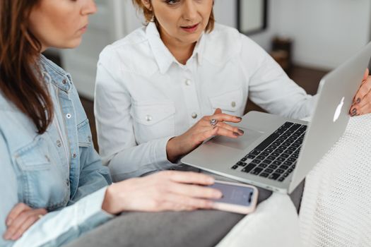 Two women working together on a laptop and smartphone indoors.